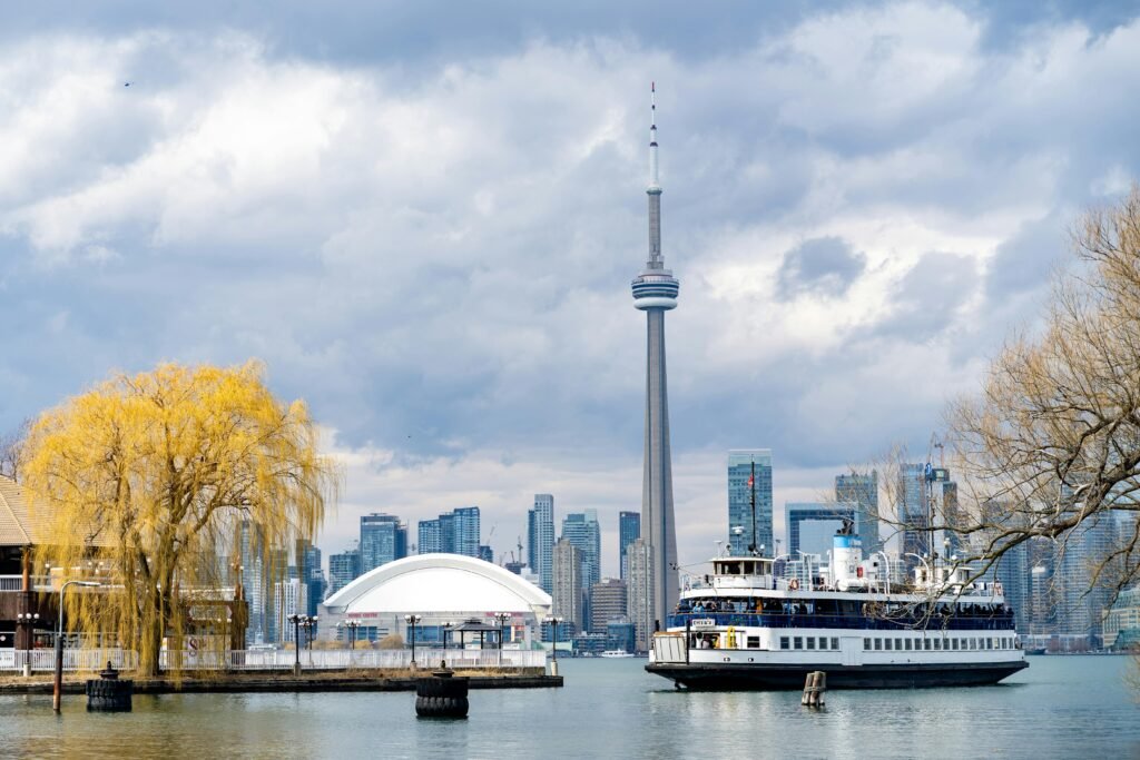 Scenic view of Toronto skyline featuring the CN Tower and a ferry on a cloudy day.