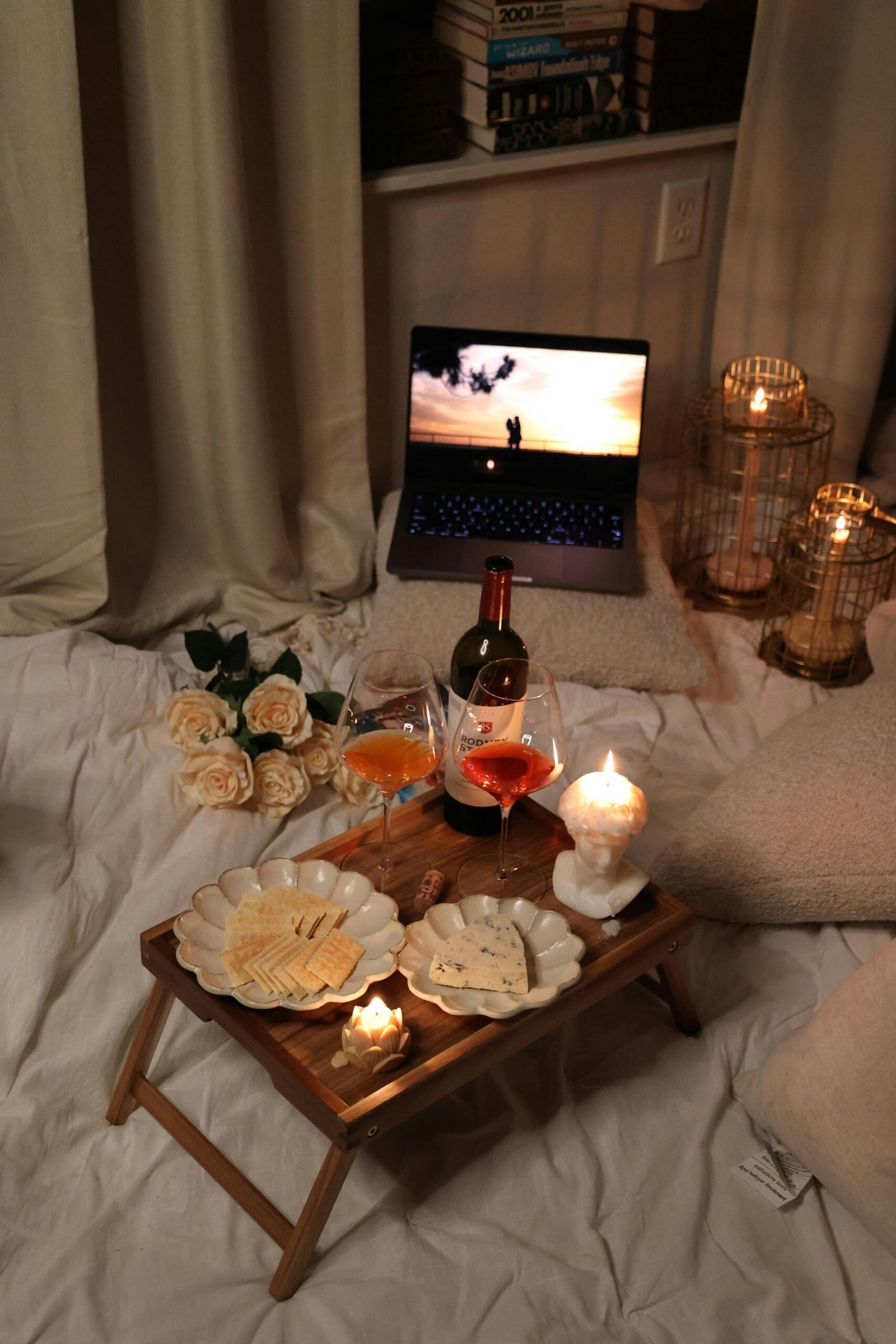 Cozy indoor setup with wine, cheeses, candles, and a relaxing laptop view.