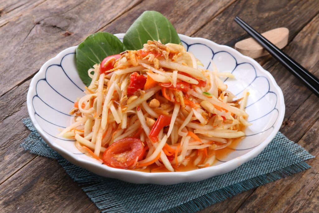 A flavorful Thai green papaya salad on rustic wooden table with chopsticks.