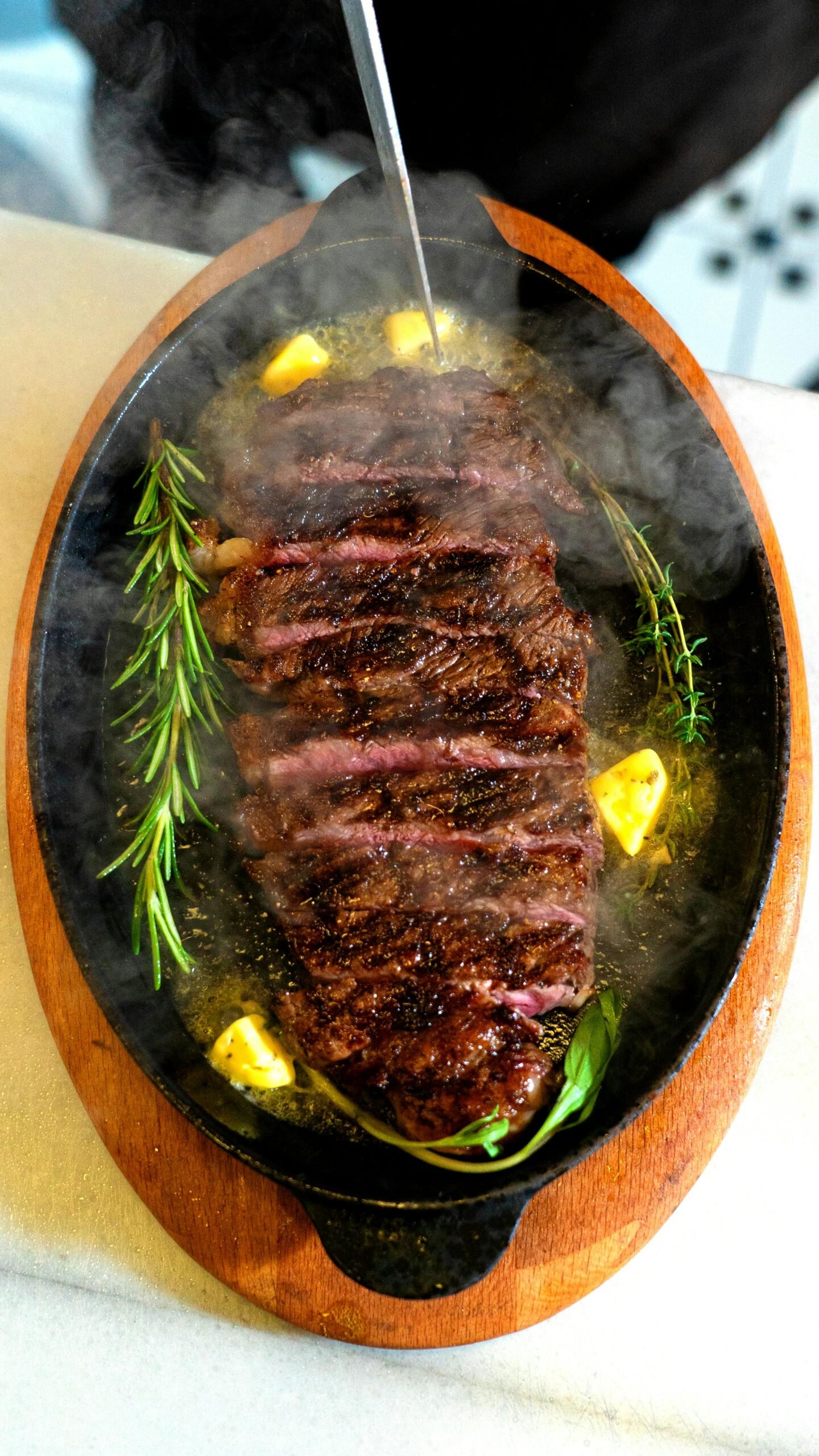 Juicy grilled steak on a wooden hot plate garnished with fresh herbs and butter.
