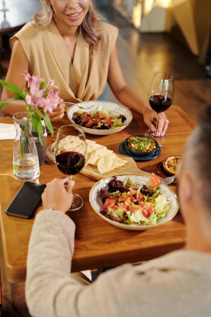 A couple enjoys a meal with wine, salads, and appetizers at a cozy restaurant.