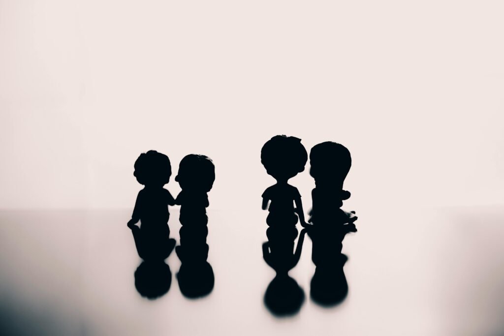 Silhouettes of cute small figurines of boys and girls placed on surface with shadow against white wall in room with bright light