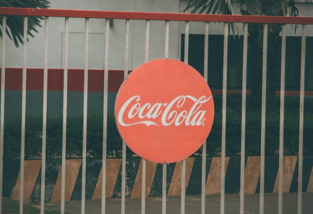 Coca-Cola logo prominently displayed on outdoor fence, urban setting.