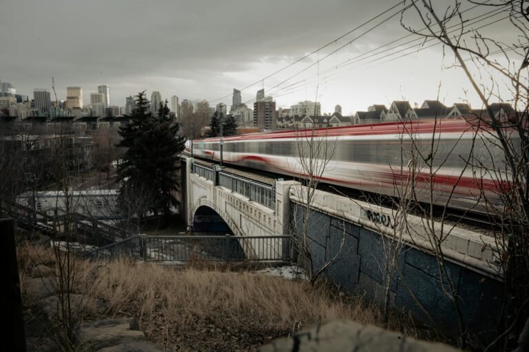 A high-speed train speeding across a bridge in Calgary with city skyline in the background.