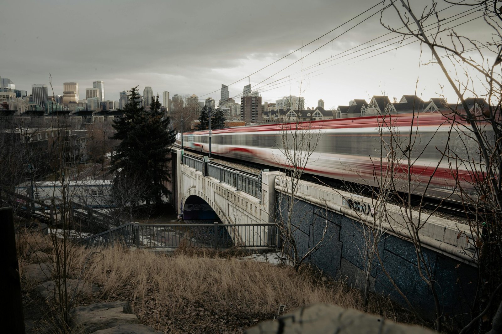 A high-speed train speeding across a bridge in Calgary with city skyline in the background.