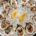 A bowl of fresh oysters on ice garnished with lemon wedges, showcasing seafood freshness.