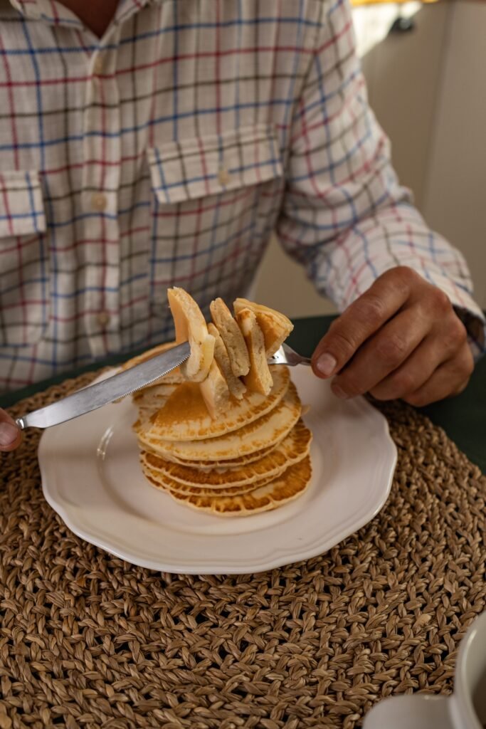 Close-up of a man in a plaid shirt slicing pancakes on a plate for breakfast.