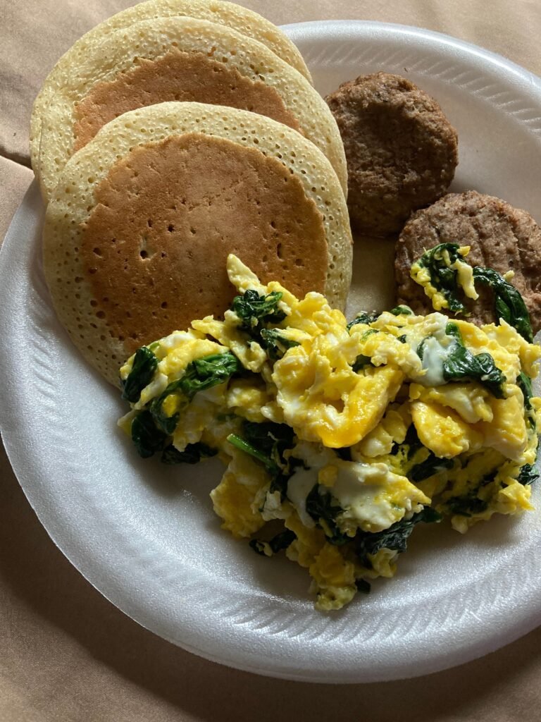Tasty homemade breakfast with pancakes, scrambled eggs, and sausage on a paper plate.