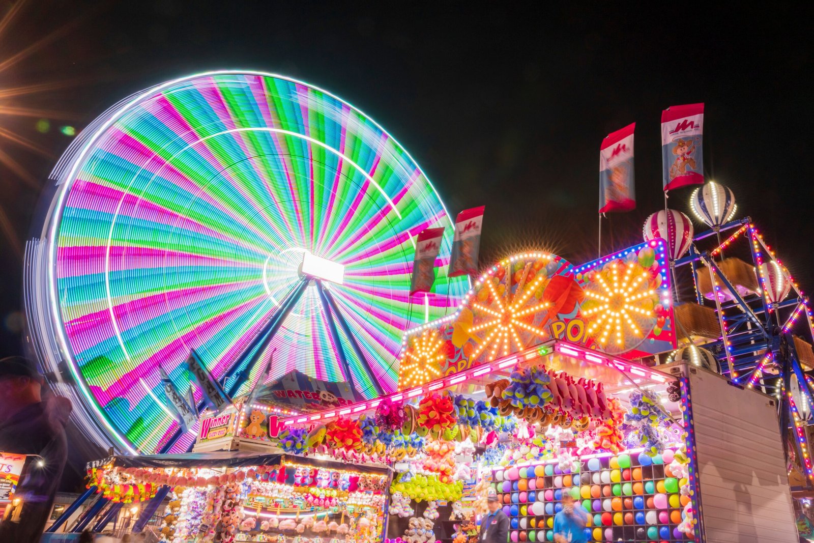 Colorful ferris wheel and stalls light up the night at an amusement park.