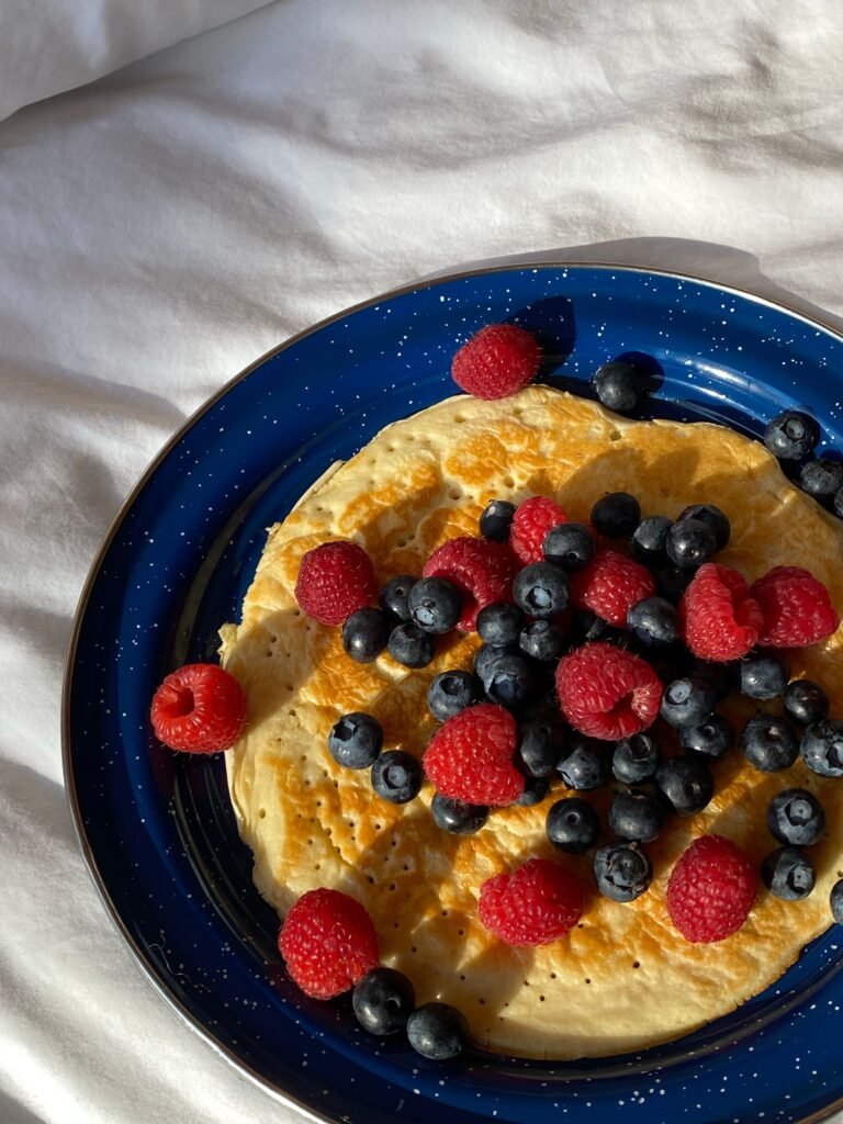 Mouth-watering pancakes topped with fresh raspberries and blueberries on a vibrant blue plate.
