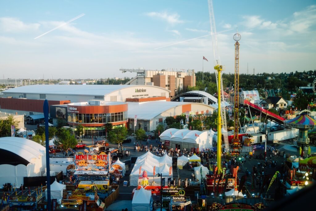 A high-angle shot of a bustling fairground with various rides and stalls under a clear sky.