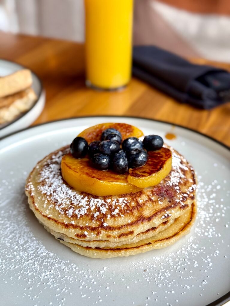 Mouth-watering pancakes topped with blueberries, orange slices, and powdered sugar, perfect for breakfast.