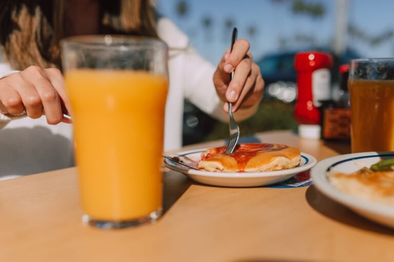 A woman dining outdoors, enjoying pancakes with syrup and a glass of orange juice.